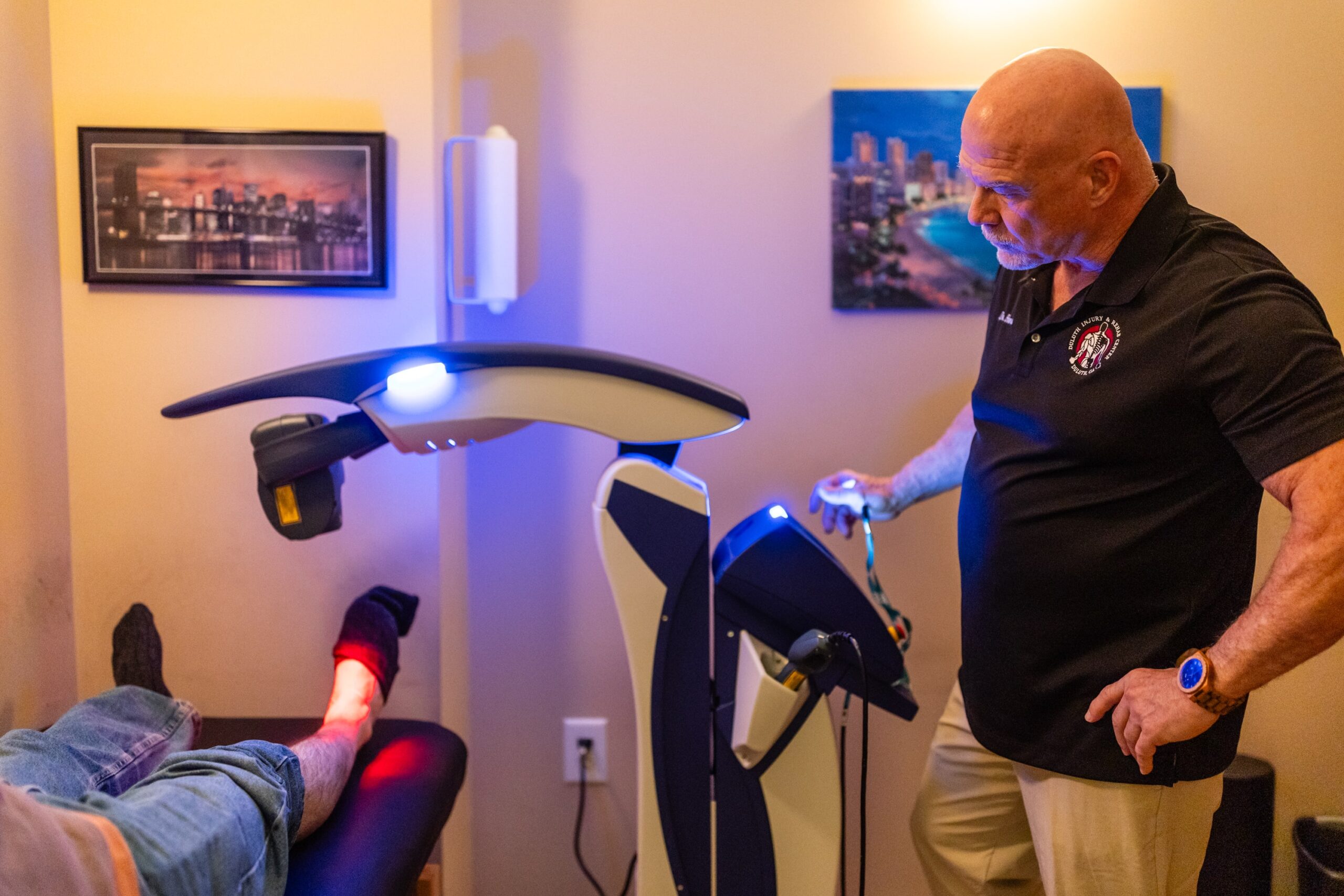A man operates a therapeutic laser device on a patient's foot in a clinical setting.