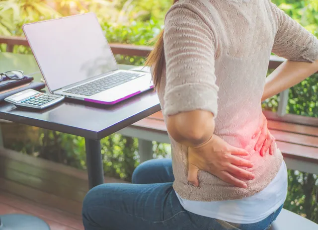 Person experiencing lower back pain while working at a laptop outdoors.